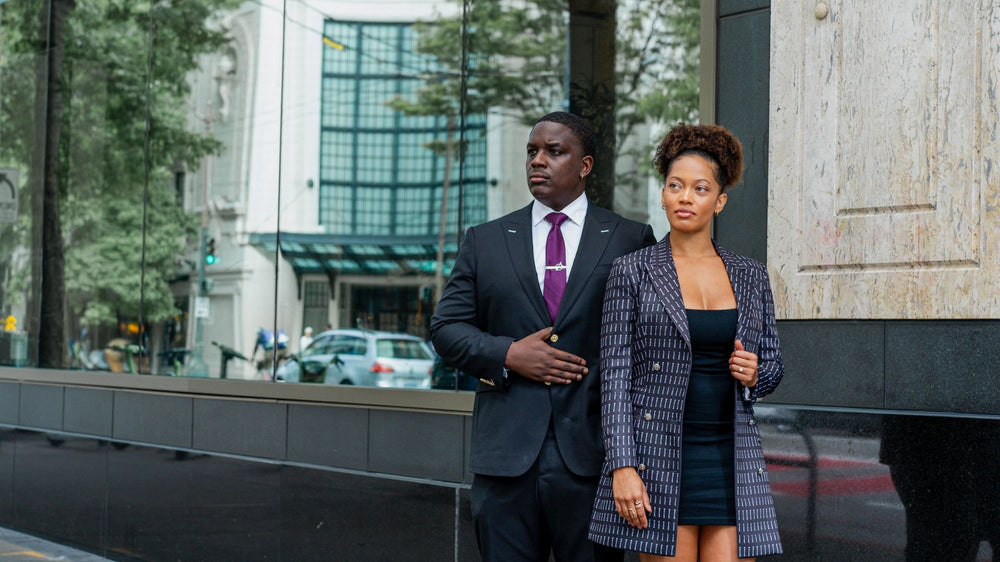Two people wearing tailored outfits outside a building