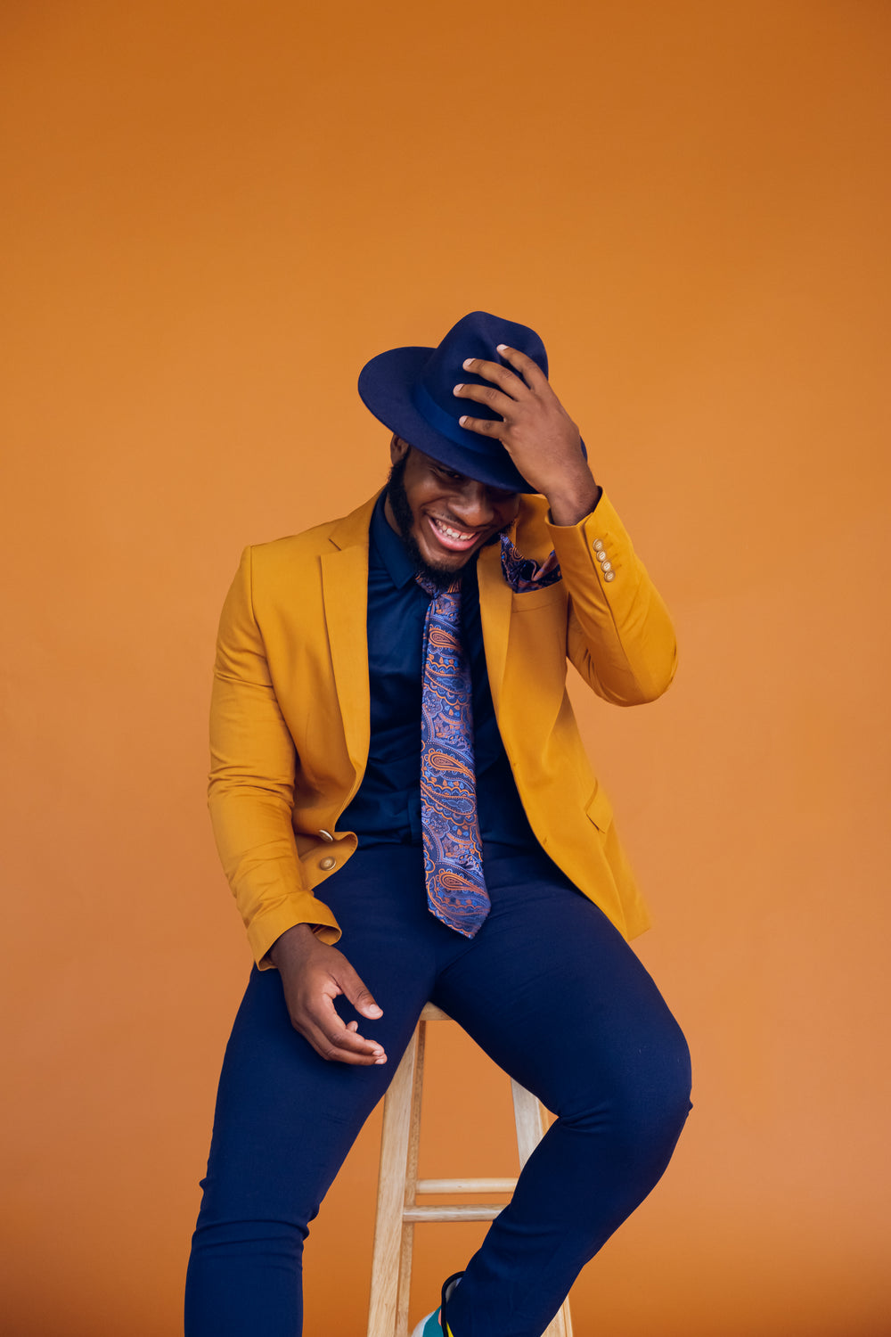 Person wearing a mustard jacket and blue hat against an orange background