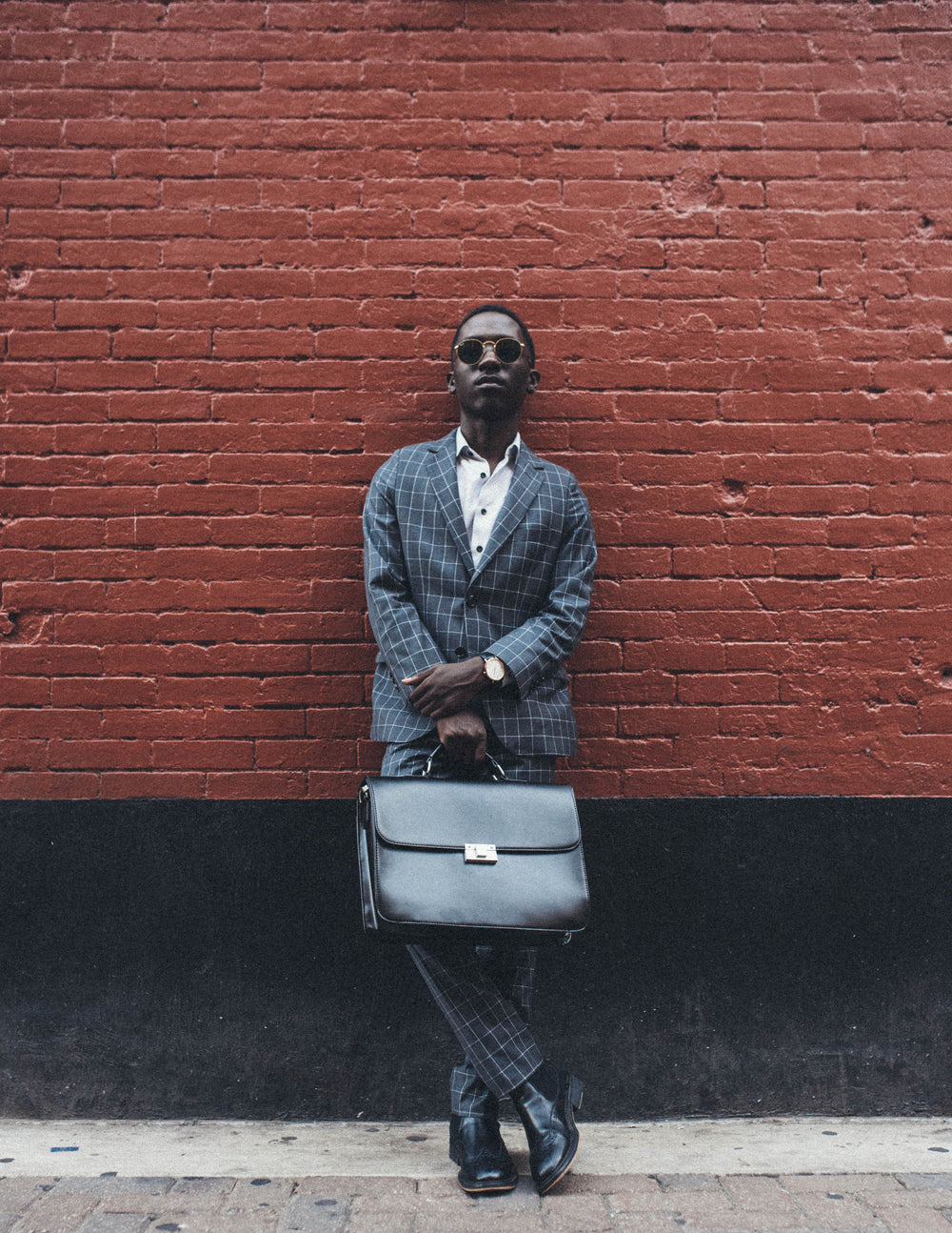 Person wearing a dark suit and carrying a briefcase beside a brick wall