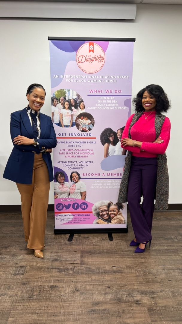 Two people standing beside a Growing Up, Black Girl event banner