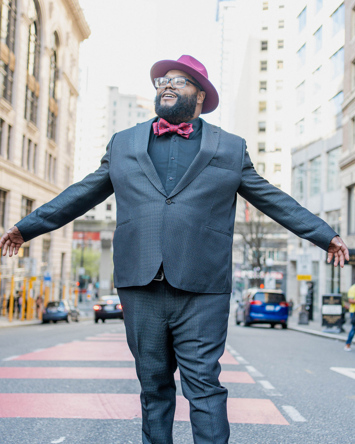 Person wearing a dark suit, bright bow tie and burgundy hat